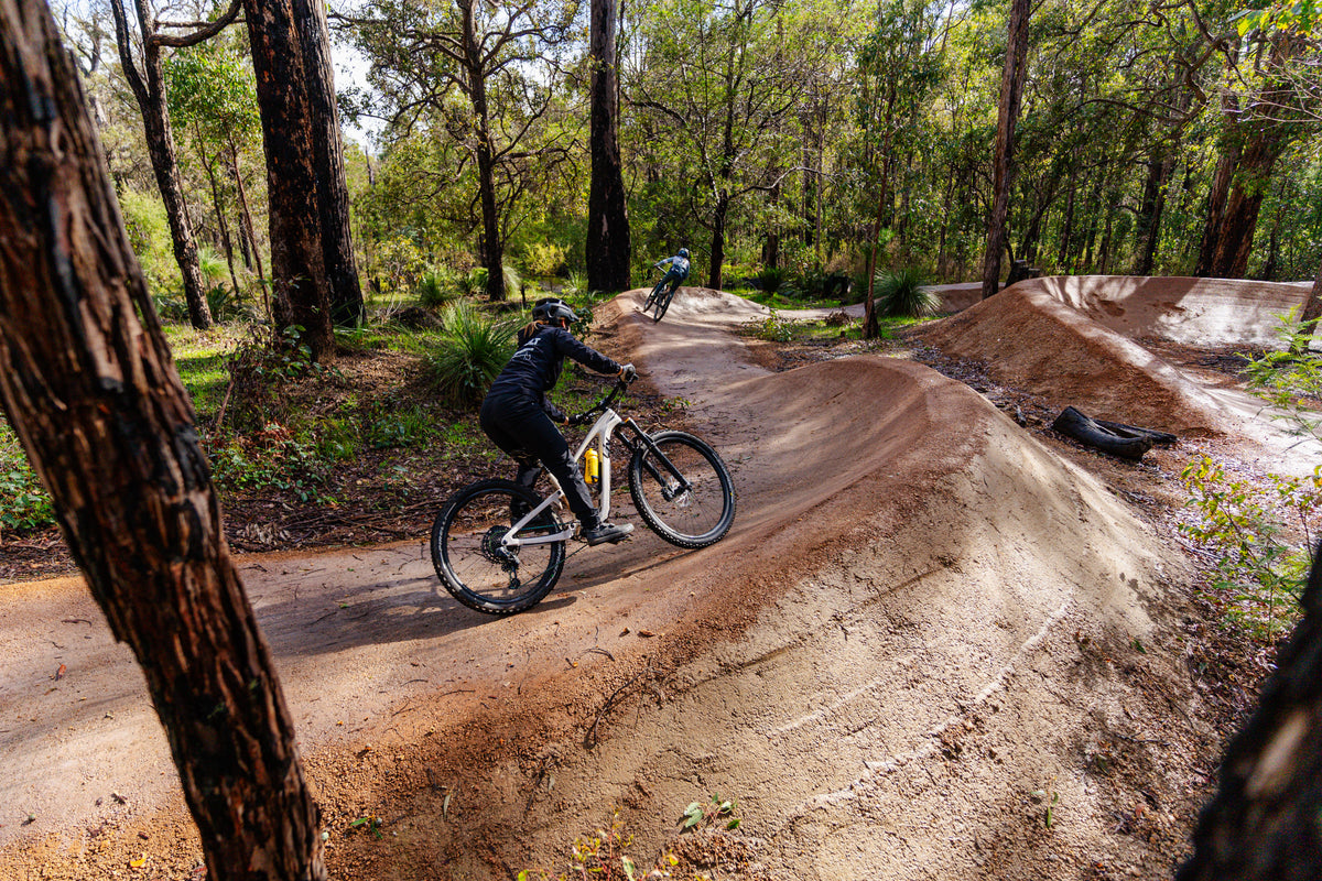Mountain Bike track and berms through forest, ridden by two mountain bikers.